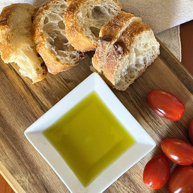 Mediterranean olive oil with rustic bread and fresh tomatoes on a wooden table, representing simple daily food rituals and sustainable Mediterranean eating habits. SOGNO by Hetty Mediterranean well-being