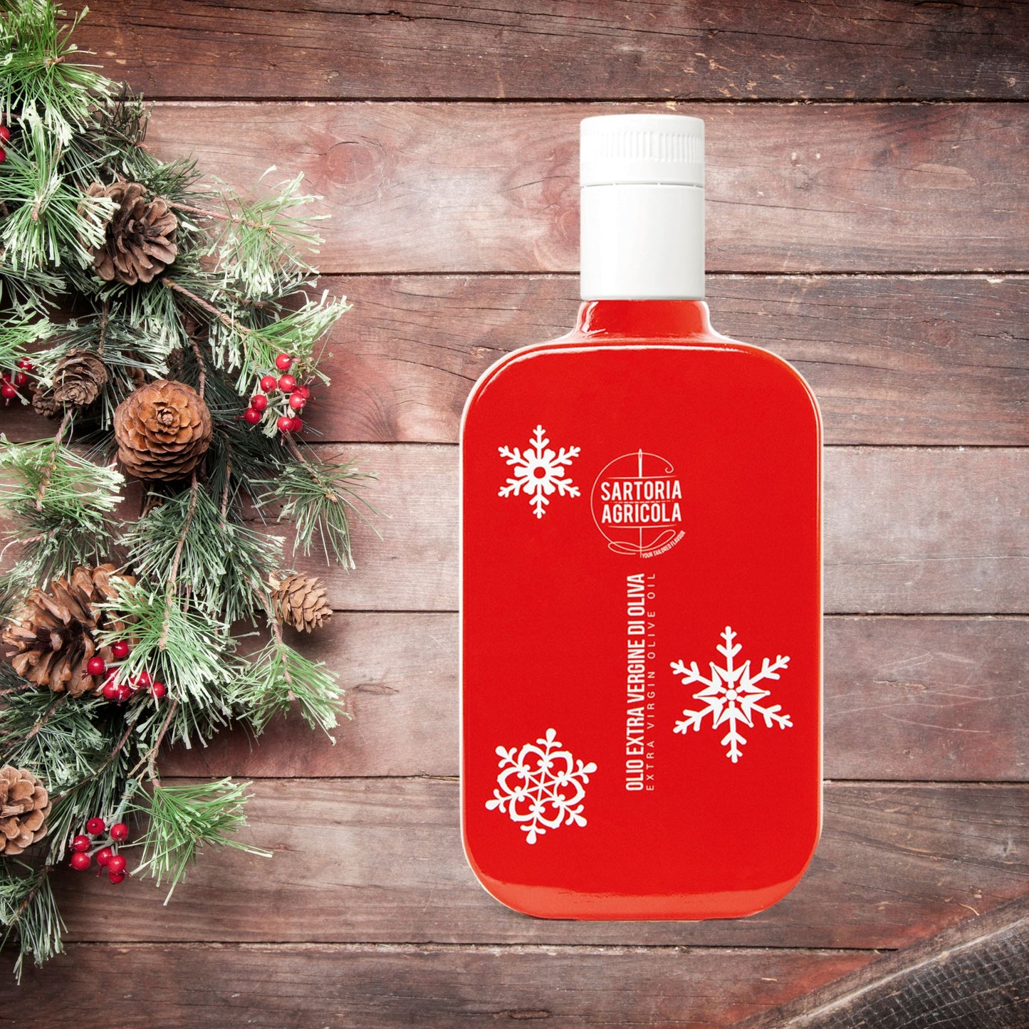 Red bottle of extra virgin olive oil, Christmas limited edition crafted in Puglia, with white snowflake design on wood background.